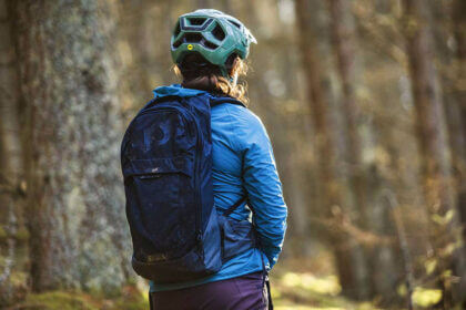 MTB hydration bag on mountain biker's back during trail ride showing water reservoir and gear storage compartments