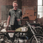 Mike Wolfe standing beside vintage motorcycle in restored workshop for his passion project