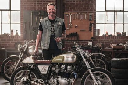 Mike Wolfe standing beside vintage motorcycle in restored workshop for his passion project