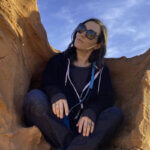 Woman sitting in desert rock formation representing Sinn Sage net worth success story