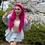 Lily Lou posing outdoors with pink hair during cherry blossom season, showcasing her social media presence that contributes to her net worth