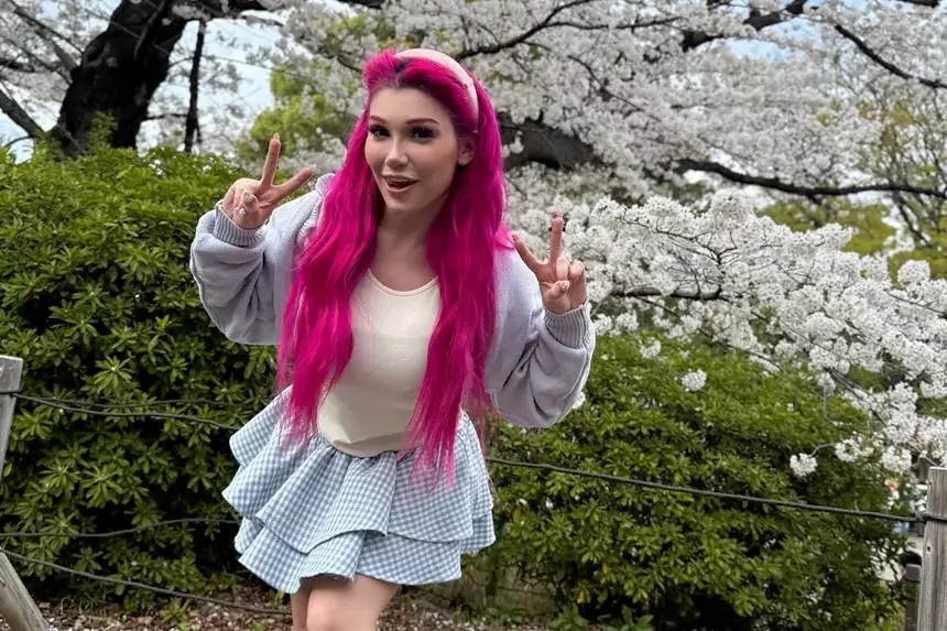 Lily Lou posing outdoors with pink hair during cherry blossom season, showcasing her social media presence that contributes to her net worth