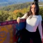 Kayla Lauren posing outdoors at a scenic mountain viewpoint with autumn foliage in the background, wearing a white long-sleeve top — Instagram model and ShagMag executive with an estimated net worth of $500K