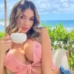 Lyna Perez holding a coffee cup at a tropical beach resort, wearing a pink bikini top