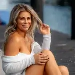 Paige VanZant smiling in a white off-shoulder top at a waterfront dock — MMA fighter and content creator with an estimated net worth of $4–6 million in 2026