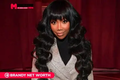 Brandy smiling in a beige blazer against a red curtain backdrop for the Brandy Net Worth article.