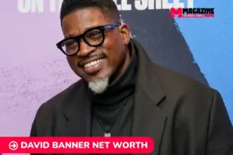 David Banner net worth portrait, smiling in glasses and black overcoat at event backdrop.